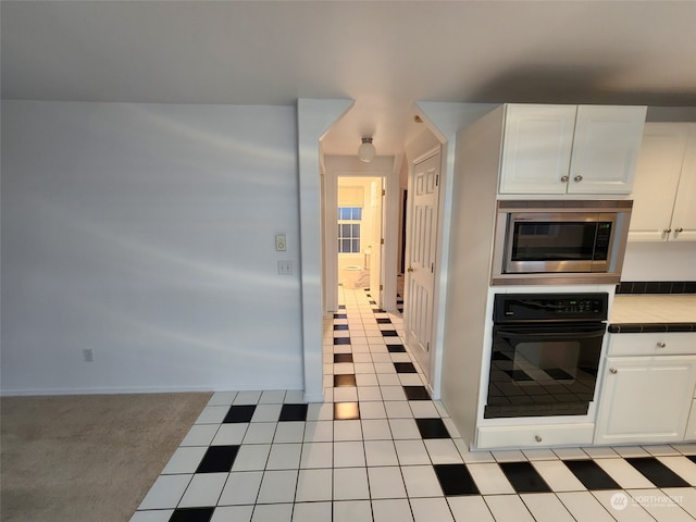 kitchen with light tile patterned flooring, white cabinetry, oven, stainless steel microwave, and tile counters