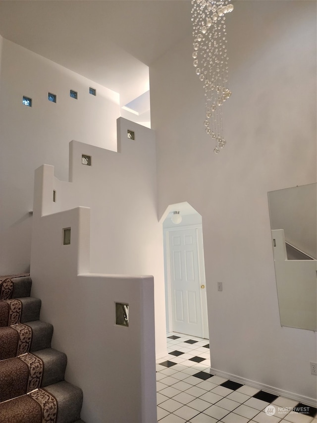 staircase with tile patterned flooring, a high ceiling, and an inviting chandelier