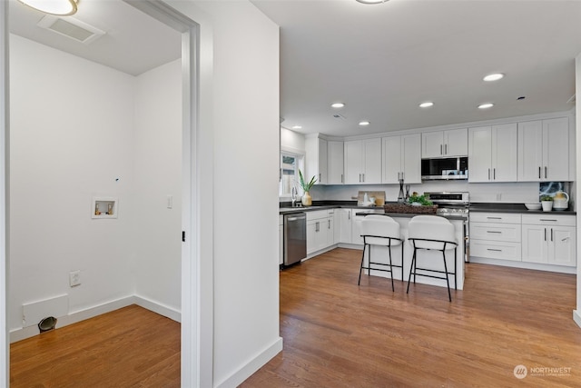 kitchen featuring a breakfast bar, a center island, white cabinets, appliances with stainless steel finishes, and light hardwood / wood-style floors