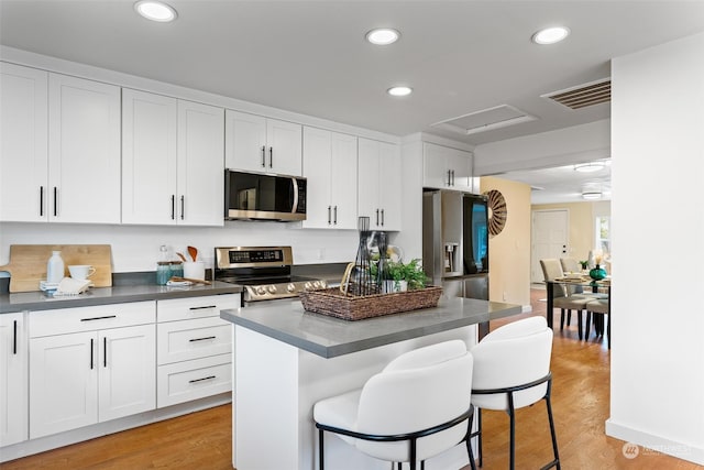 kitchen with a breakfast bar, a center island, white cabinets, light wood-type flooring, and appliances with stainless steel finishes