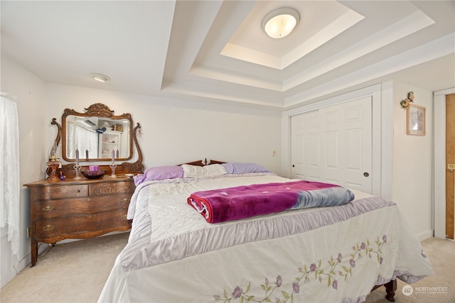 carpeted bedroom with a closet and a raised ceiling