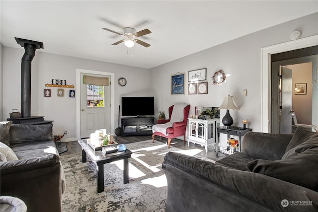 living room with wood-type flooring, a wood stove, and ceiling fan