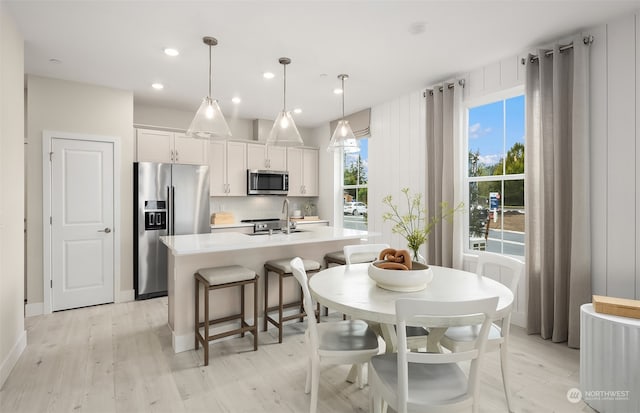 kitchen featuring a kitchen island with sink, white cabinets, hanging light fixtures, and stainless steel appliances