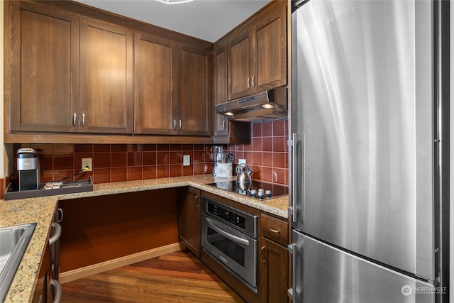 kitchen with backsplash, dark hardwood / wood-style flooring, light stone counters, and appliances with stainless steel finishes