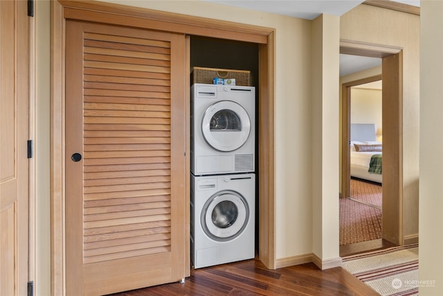 laundry room with stacked washer / drying machine and dark wood-type flooring