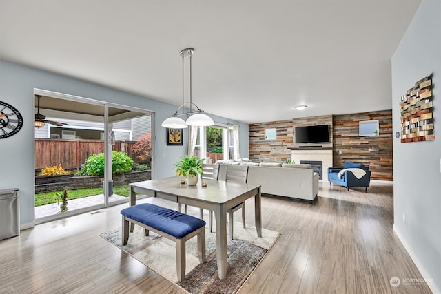 dining area with a large fireplace, ceiling fan, light hardwood / wood-style floors, and wood walls