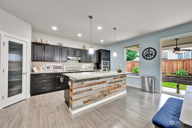 kitchen with decorative backsplash, hanging light fixtures, ceiling fan, appliances with stainless steel finishes, and light hardwood / wood-style flooring