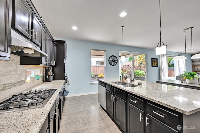 kitchen featuring appliances with stainless steel finishes, sink, an island with sink, pendant lighting, and light hardwood / wood-style flooring