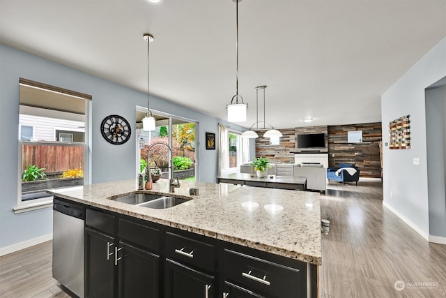 kitchen with a kitchen island with sink, light hardwood / wood-style flooring, dishwasher, wooden walls, and sink