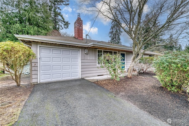 single story home with an attached garage, a chimney, and aphalt driveway