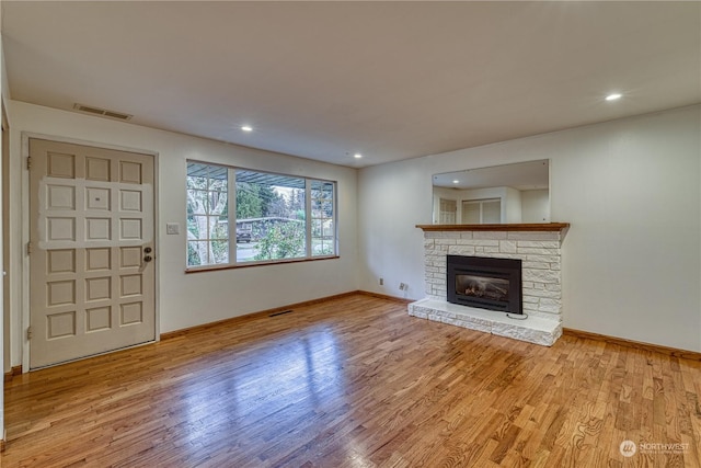 unfurnished living room featuring a stone fireplace, light wood-type flooring, visible vents, and baseboards