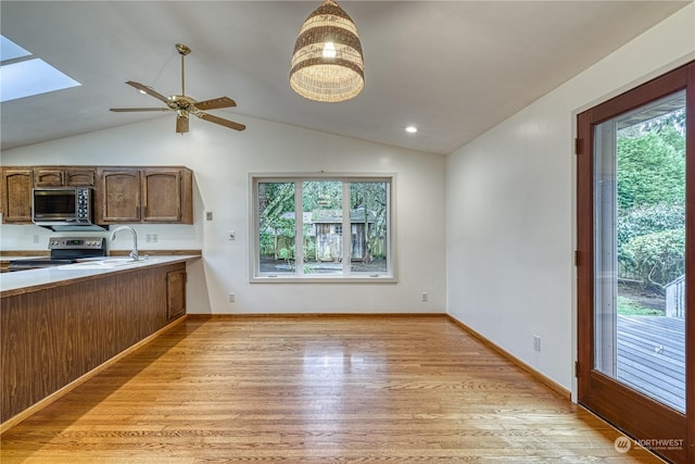 kitchen with lofted ceiling with skylight, light wood-style flooring, brown cabinets, stainless steel electric stove, and light countertops