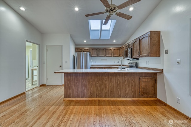 kitchen featuring brown cabinets, stainless steel appliances, light countertops, a sink, and a peninsula