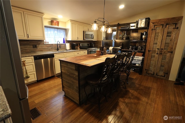 kitchen featuring appliances with stainless steel finishes, decorative light fixtures, sink, vaulted ceiling, and a center island