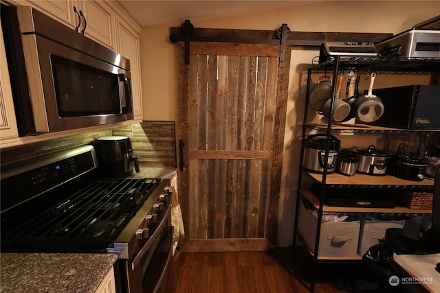 kitchen with dark wood-type flooring, dark stone counters, and appliances with stainless steel finishes