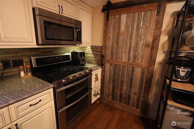 kitchen with stainless steel appliances, cream cabinets, dark stone countertops, dark wood-type flooring, and decorative backsplash