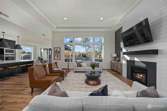 living room featuring dark hardwood / wood-style flooring, wood walls, a large fireplace, and a raised ceiling