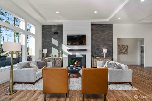 living room with a tray ceiling, hardwood / wood-style flooring, and a large fireplace