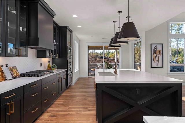 kitchen with sink, appliances with stainless steel finishes, decorative light fixtures, and a center island with sink