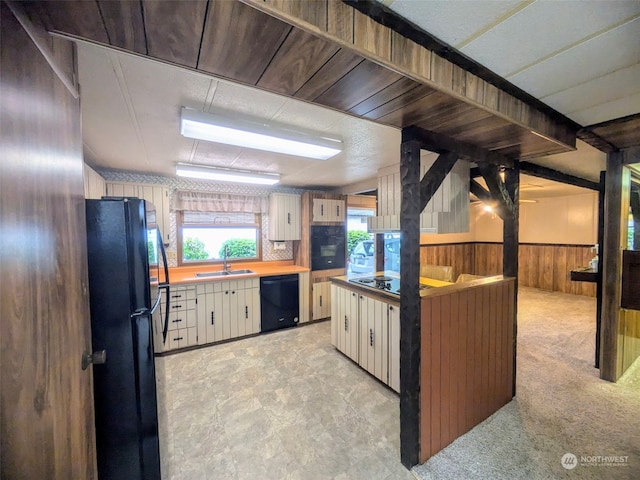 kitchen featuring light colored carpet, black appliances, sink, wooden walls, and white cabinetry