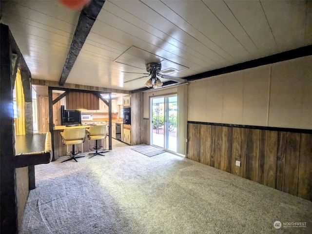 interior space featuring light colored carpet, wood walls, ceiling fan, and beam ceiling