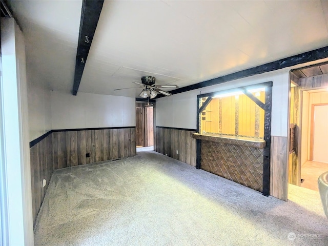 carpeted empty room with wood walls, beamed ceiling, and ceiling fan