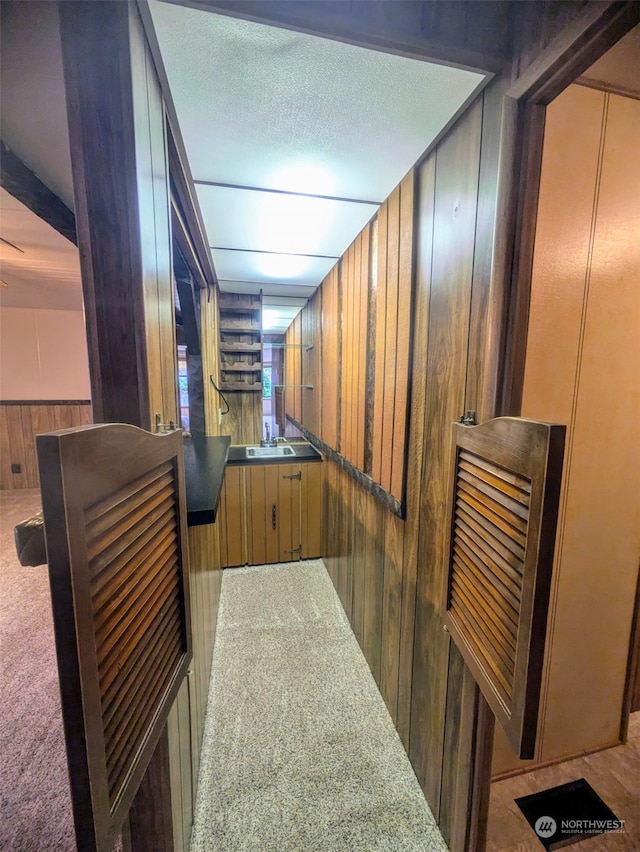 corridor featuring wooden walls, carpet flooring, a textured ceiling, and sink