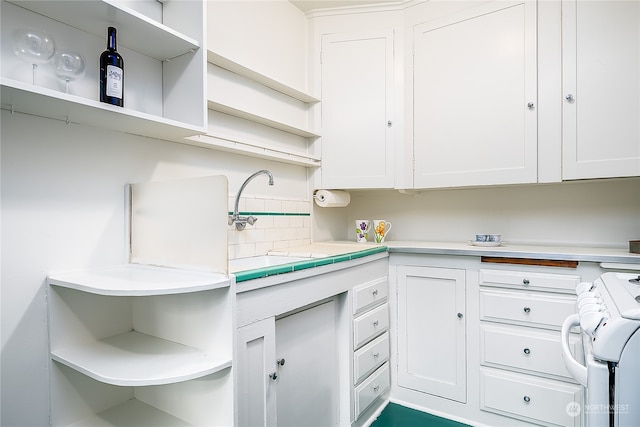 kitchen featuring white cabinets, stove, decorative backsplash, and sink