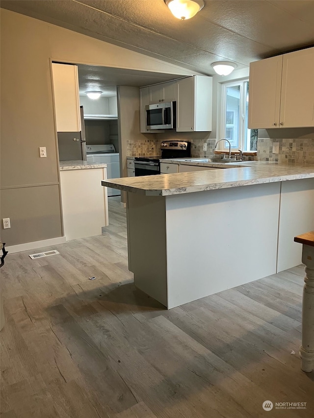 kitchen with white cabinetry, kitchen peninsula, appliances with stainless steel finishes, lofted ceiling, and washing machine and dryer