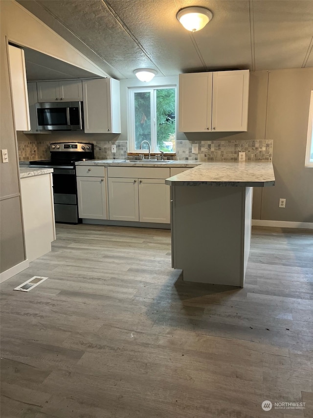 kitchen with white cabinets, light wood-type flooring, appliances with stainless steel finishes, and a kitchen island