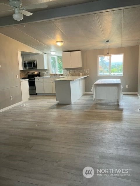 kitchen featuring a wealth of natural light, appliances with stainless steel finishes, white cabinets, and decorative light fixtures