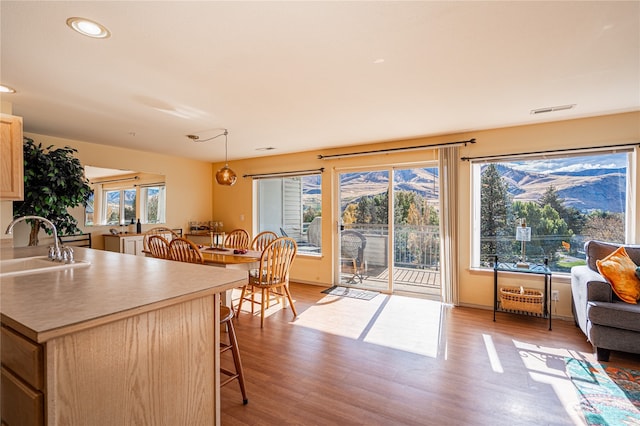 kitchen with light brown cabinets, a kitchen breakfast bar, light hardwood / wood-style flooring, sink, and decorative light fixtures