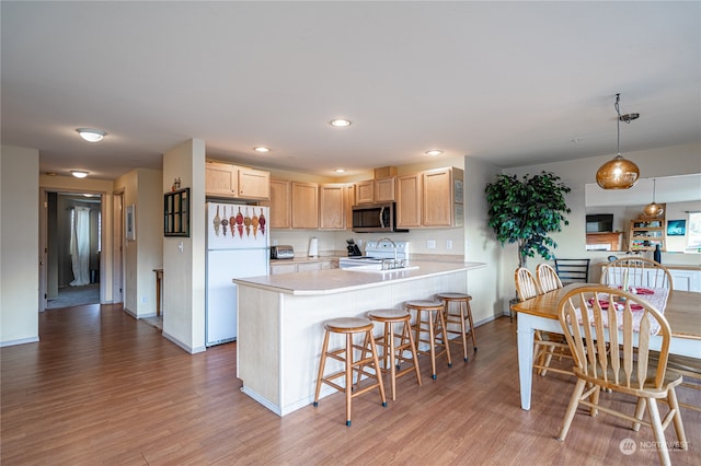 kitchen with light brown cabinets, light hardwood / wood-style flooring, pendant lighting, and white appliances