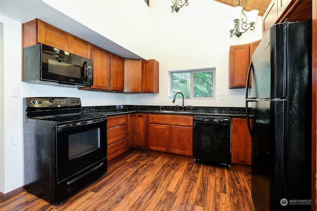 kitchen featuring black appliances, dark stone counters, hanging light fixtures, sink, and dark wood-type flooring