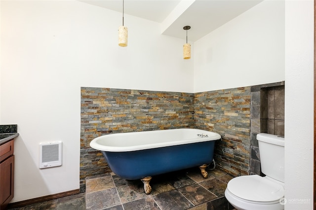 bathroom with a tub to relax in, heating unit, vanity, toilet, and tile walls