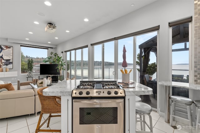 kitchen featuring a kitchen bar, stainless steel range with gas stovetop, light tile patterned flooring, and light stone counters