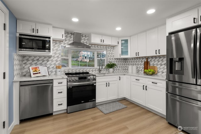 kitchen featuring stainless steel appliances, sink, wall chimney range hood, white cabinetry, and light wood-type flooring