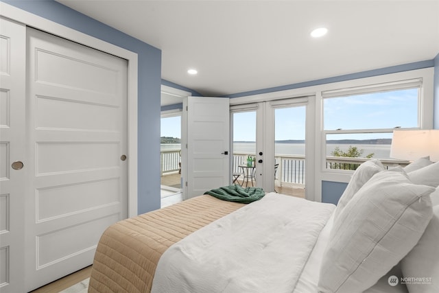 bedroom featuring french doors, access to outside, a water view, and light wood-type flooring