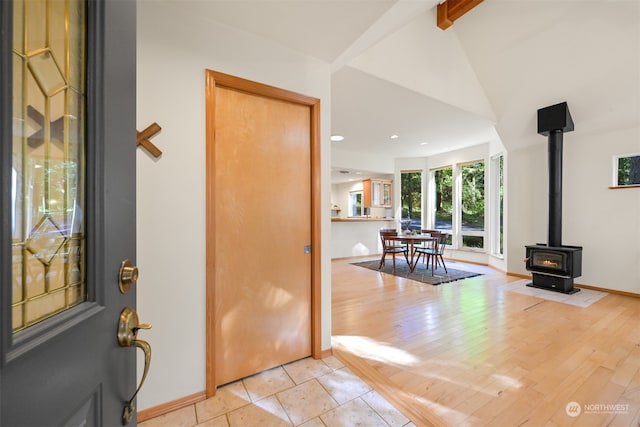 entrance foyer with vaulted ceiling with beams, a wood stove, and light wood-type flooring