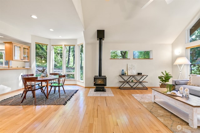 dining space featuring a wood stove, lofted ceiling, light wood-type flooring, and a wealth of natural light