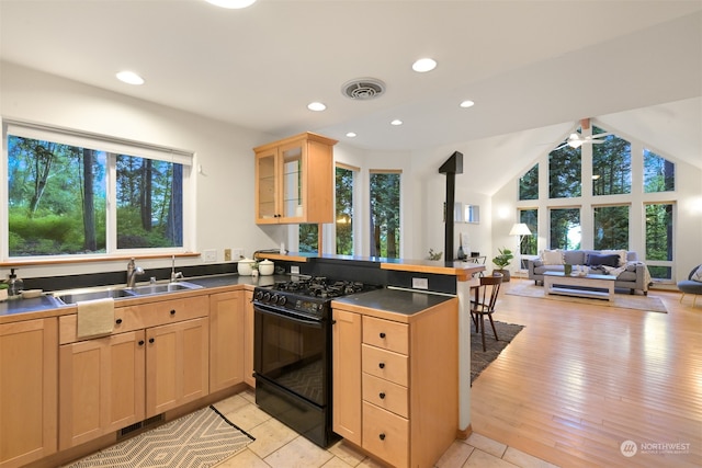 kitchen featuring kitchen peninsula, sink, vaulted ceiling, light wood-type flooring, and black gas range oven