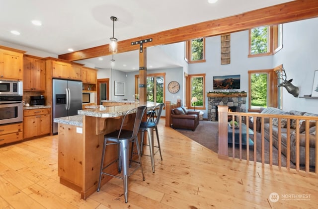 kitchen with beam ceiling, light wood-style flooring, appliances with stainless steel finishes, and a fireplace