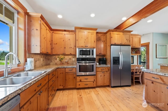 kitchen with light wood finished floors, a sink, light countertops, appliances with stainless steel finishes, and tasteful backsplash