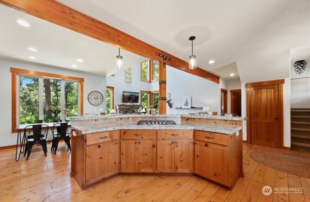 kitchen with hanging light fixtures, light wood-style flooring, light stone counters, and stainless steel gas cooktop