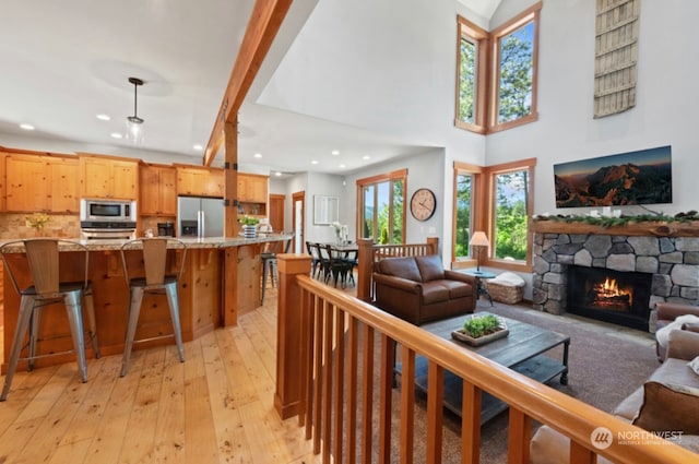 living area featuring a stone fireplace, a high ceiling, recessed lighting, and light wood-type flooring