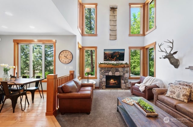 living room with a stone fireplace, a healthy amount of sunlight, light wood-type flooring, and a high ceiling