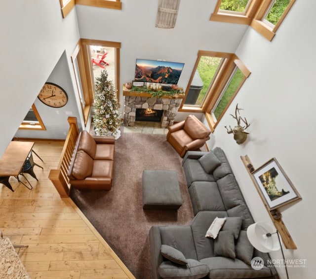 living area with a high ceiling, a stone fireplace, and hardwood / wood-style floors