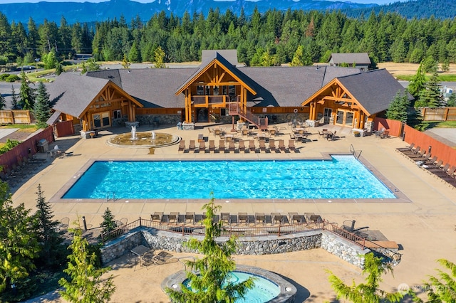 pool featuring a patio area, a mountain view, a forest view, and fence