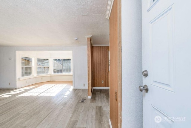 interior space with baseboards, visible vents, ornamental molding, a textured ceiling, and light wood-type flooring