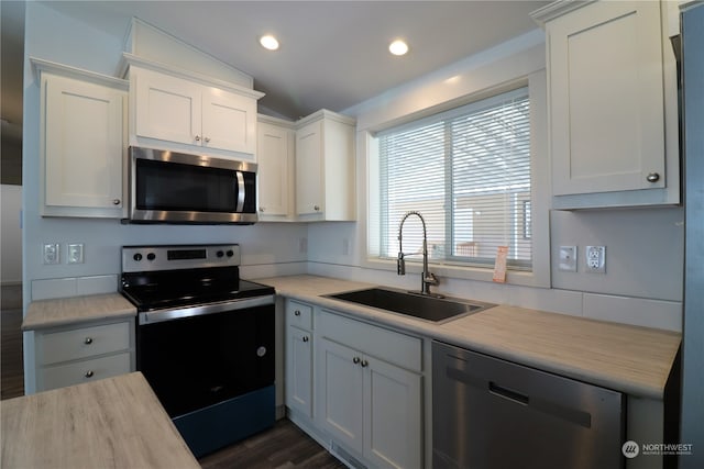 kitchen featuring white cabinets, dark hardwood / wood-style flooring, appliances with stainless steel finishes, vaulted ceiling, and sink